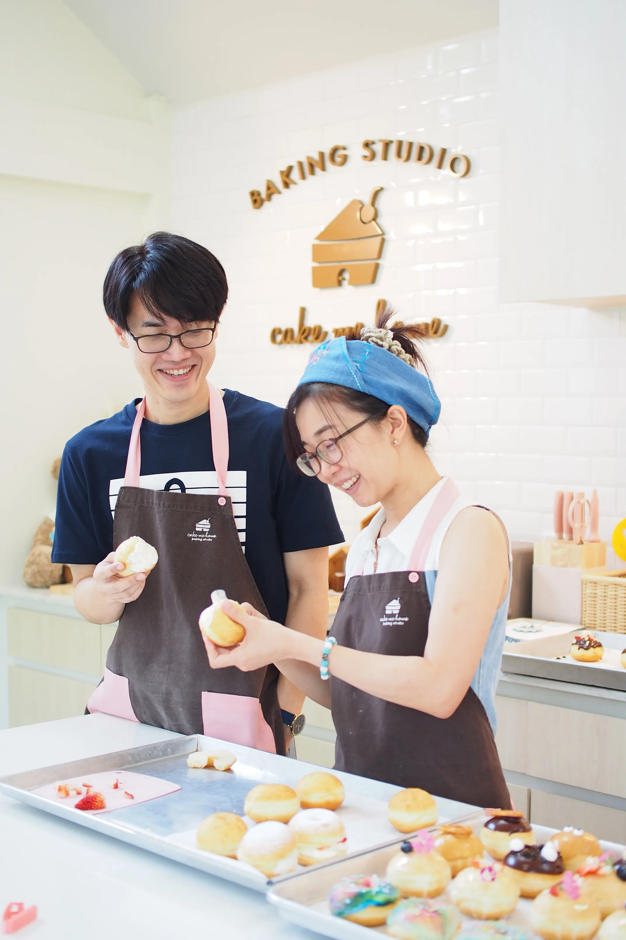 นักเรียนถือโดนัทไส้ครีมหน้าป้ายสตูดิโอ Cake Me Home
