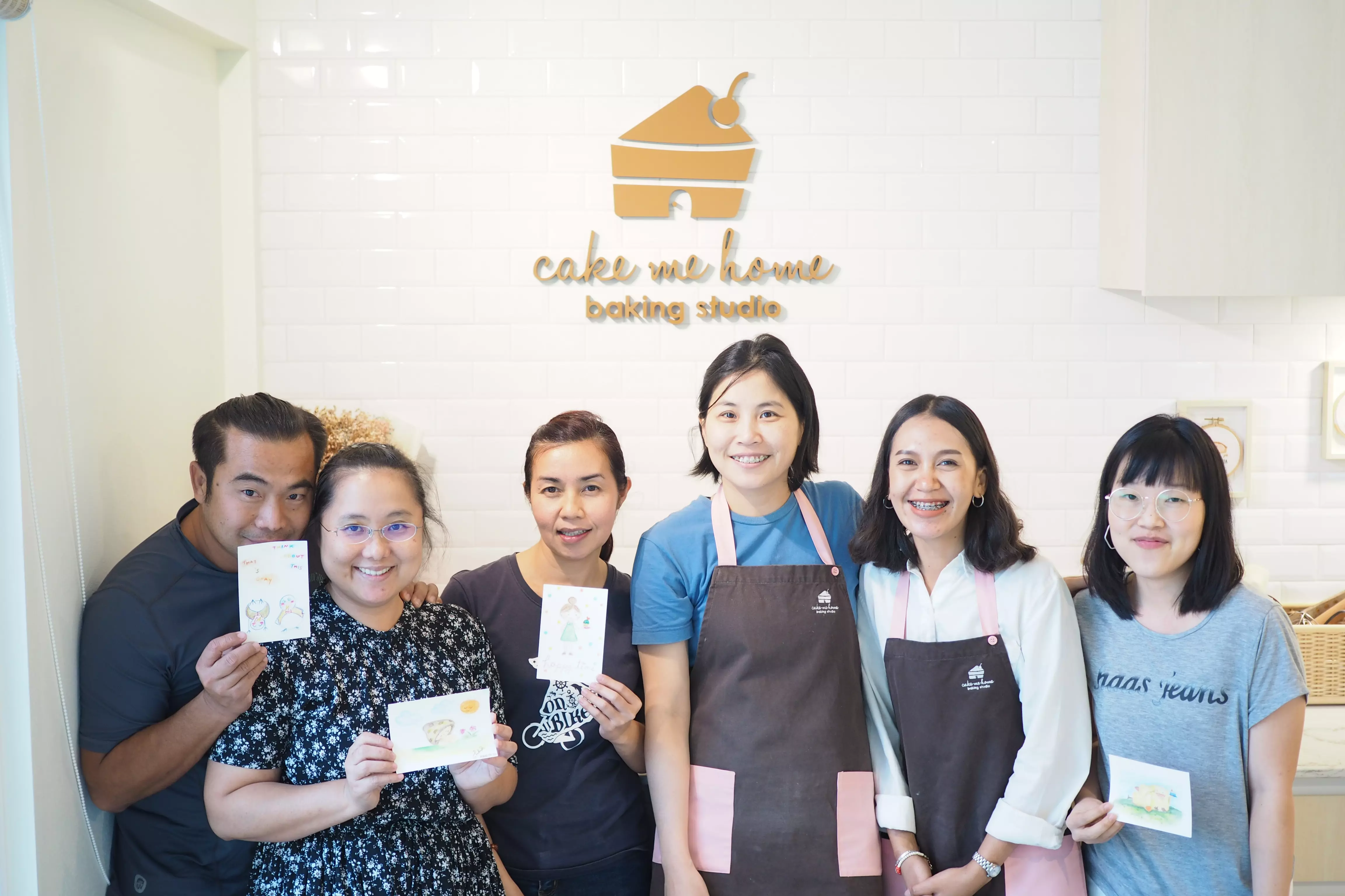 ผู้เรียนหกคนโชว์โปสการ์ดใต้โลโก้ร้าน