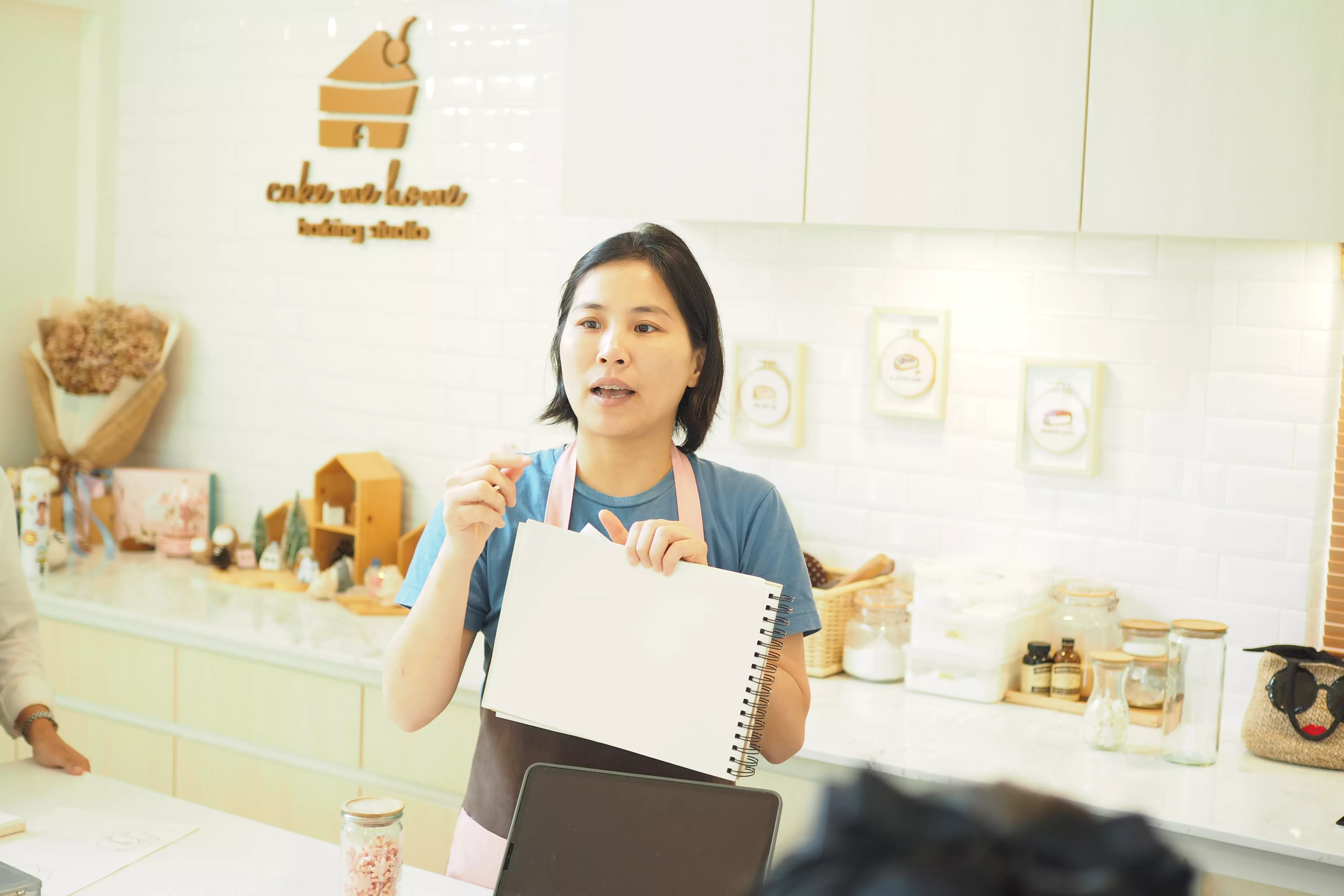ผู้สอนนำเสนอสมุดสเก็ตช์ใต้โลโก้ร้าน